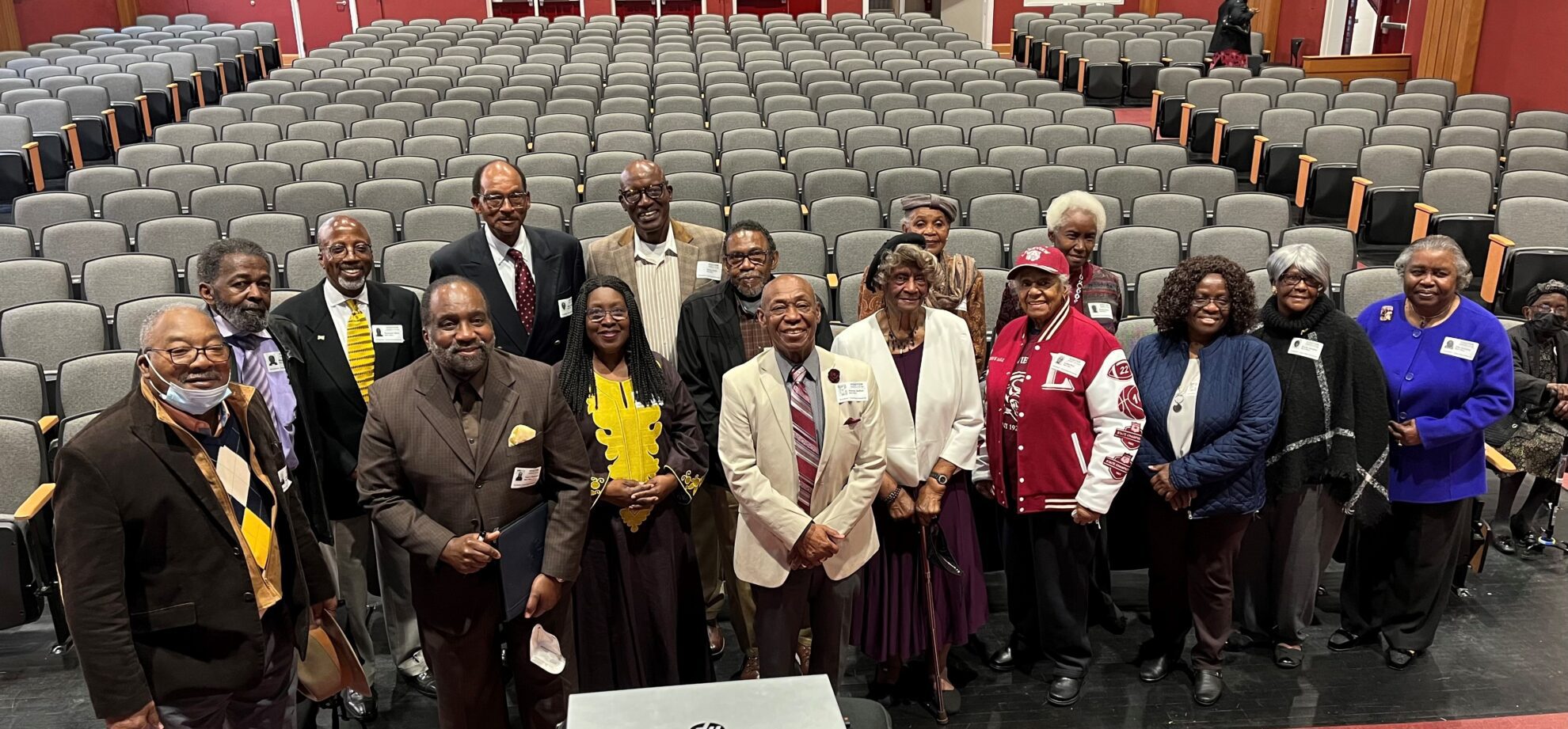 group of elderly adults stand for a photo in front of auditorium seats 
